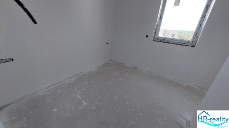 Empty room with gray-white flooring, a window, and white walls in a recreational apartment.