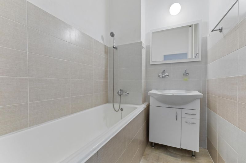 A bathroom with a bathtub, white sink, and mirror in a 3-room apartment.