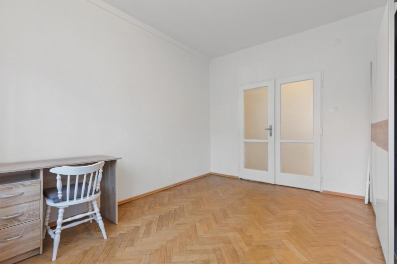 A room in a 3-bedroom apartment with a desk, a white chair, and a floor with a wooden decor.
