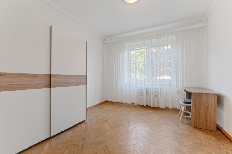 Spacious room with wood-patterned flooring, built-in wardrobe, and large window in a three-room apartment.
