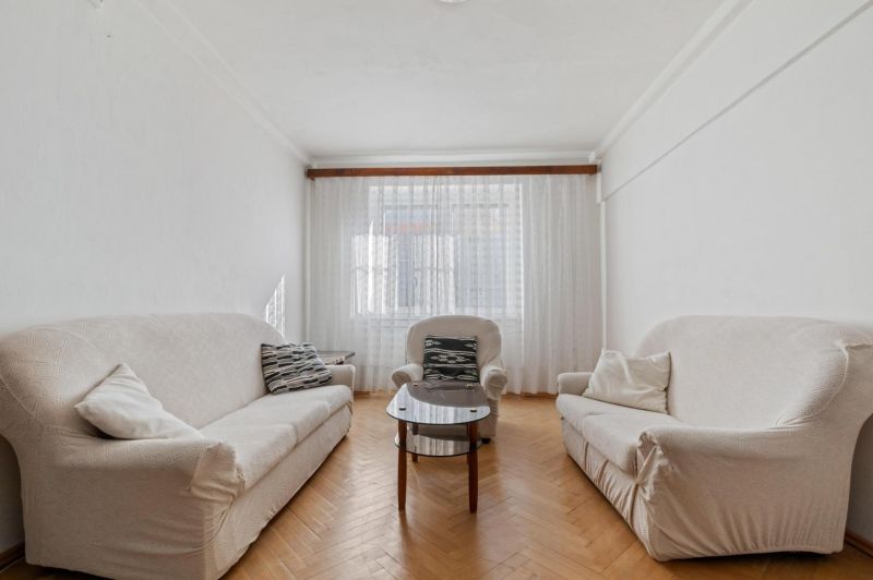 Living room with sofas, an armchair, and a wooden decor floor in a three-room apartment.