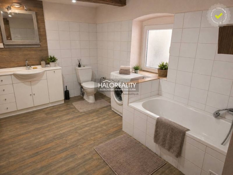 A bathroom in a family house with a washing machine, a bathtub, and a floor with a wooden decor.