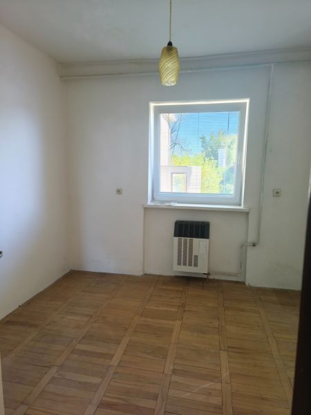 A room with a wooden floor, white walls, and a window in a family house.