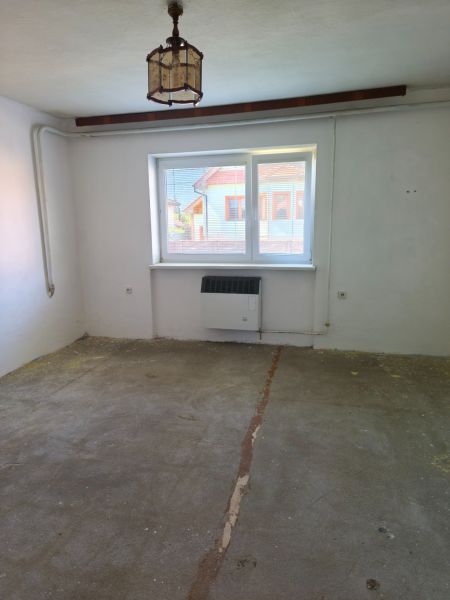 A room with one window, a light fixture, and a concrete floor in a family house.