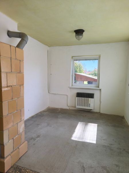 A room in a family house with a stove and a window, without floor decoration.
