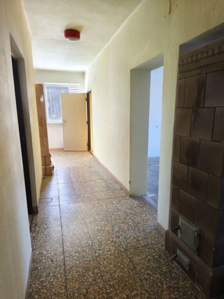 A hallway in a family house with a tiled stove and a window at the end.