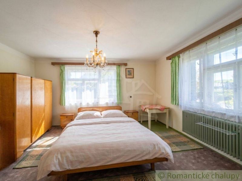 A bedroom in a family house with a wardrobe, bed, and chandelier, illuminated by natural light.