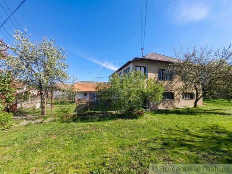 A family house in Kriváň surrounded by fruit trees and a manicured lawn under a clear sky.
