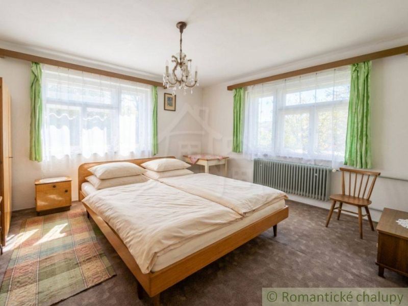Bedroom in a family house with a bed, carpet, and large windows with green curtains.