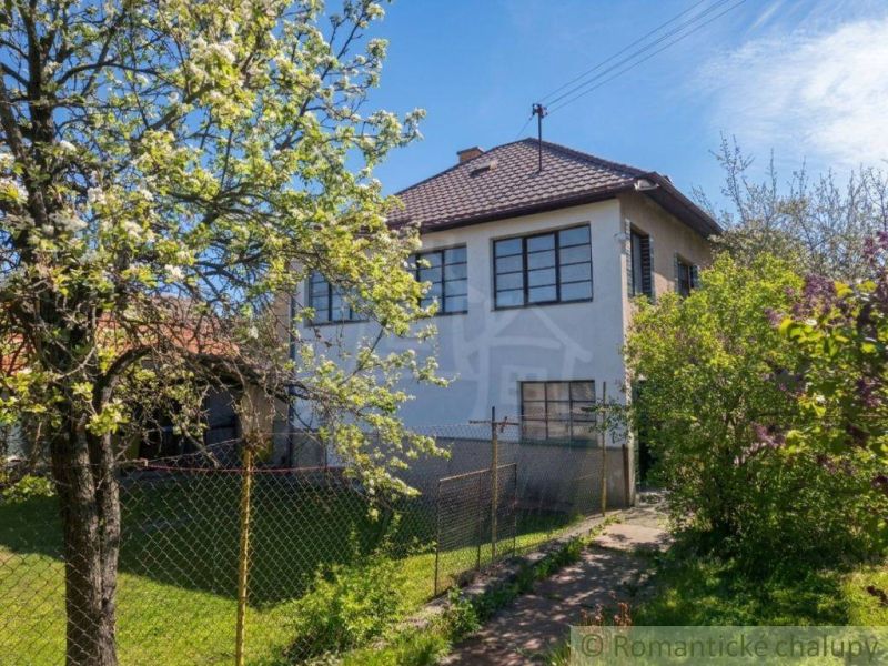 A family house in Kriváň with a front garden, a blooming tree, and a blue sky.