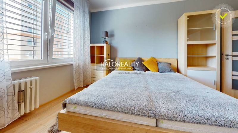 A bright bedroom in a two-room apartment with wood-patterned flooring and a large window.