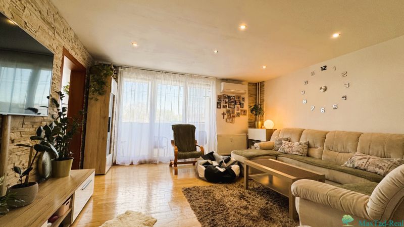 Living room with comfortable seating, large wall clock, and floor with wooden decor.