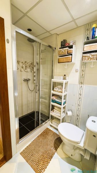 Bathroom with a shower and toilet in a 3-room apartment, shelves with stored accessories.