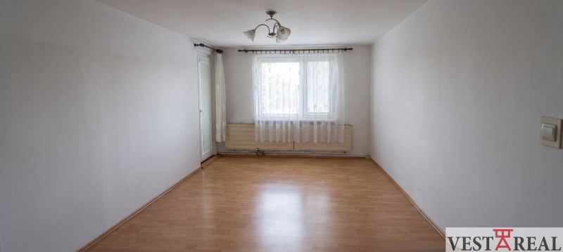 An empty room with a wooden floor and curtains in a 3-room apartment.
