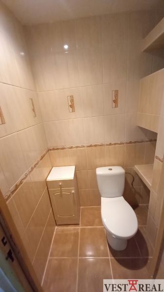 A toilet with beige tiles in a 3-room apartment.