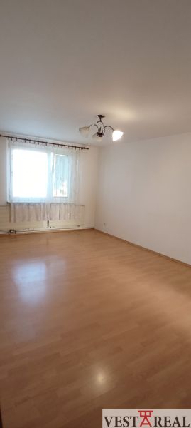 A room with a wooden decor floor in a 3-room apartment, light walls, and a window with a curtain.