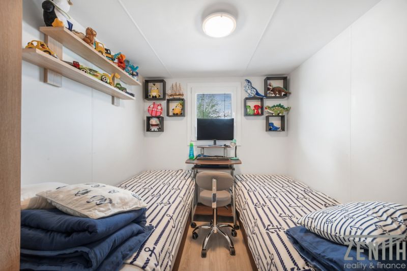 A children's room in a cottage with beds and toys on shelves, with a wooden decor floor.