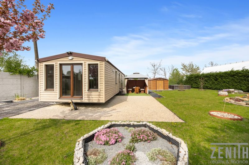 A cottage in Hurbanovo with a blooming garden, a gazebo, and a gravel path.