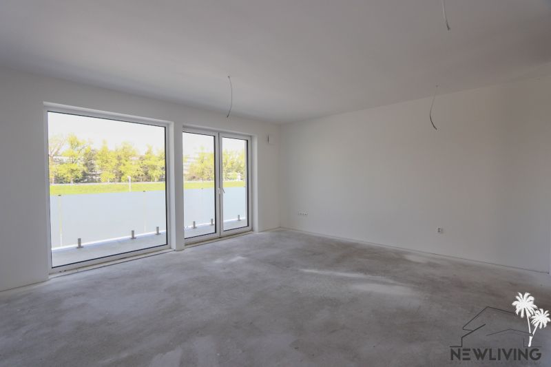 Empty room with large windows in a 2-room apartment and a view of a green area.