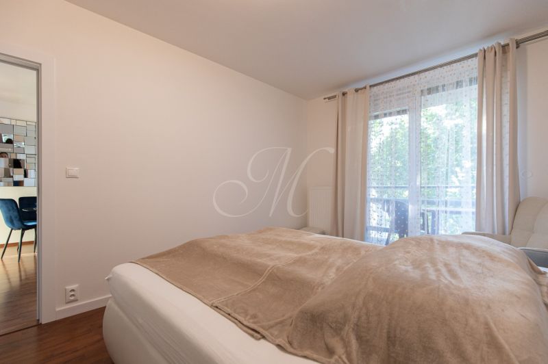 Bedroom with a bed and a window, floor with wooden decor, light curtains in a 2-room apartment.
