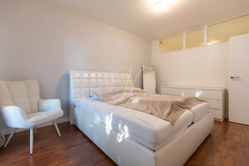 A bedroom with a white bed, an armchair, and a wooden decor floor.