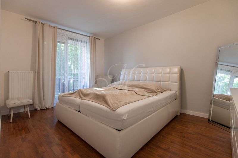 A bedroom in a 2-room apartment with a white bed and a wooden decor floor.