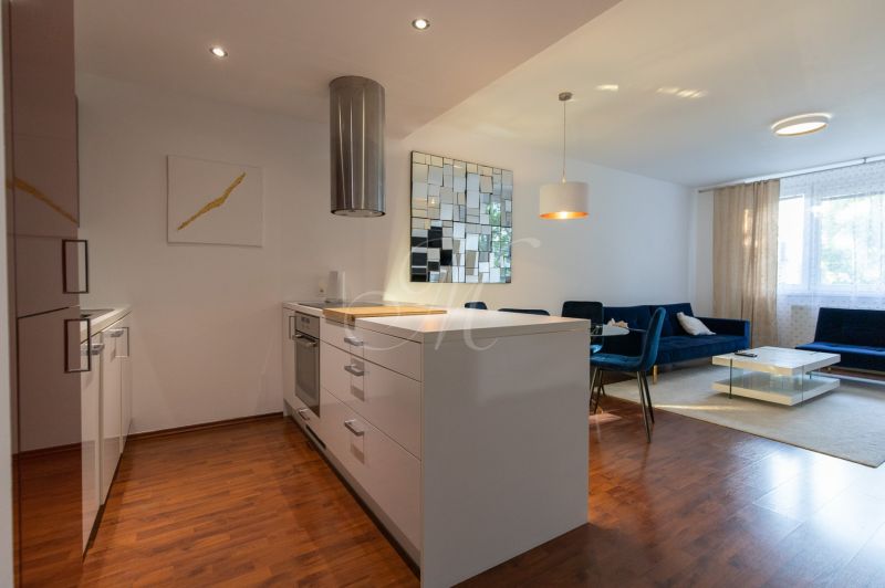 Living room with kitchen in a 2-room apartment, wooden decor flooring, white furniture.
