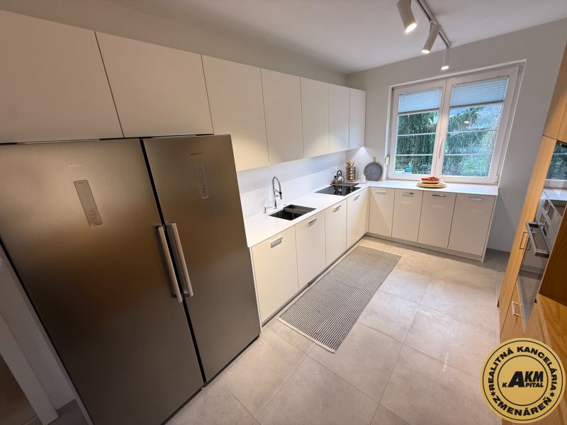 A kitchen in a family house with white cabinets, a stainless steel refrigerator, and a window with a view.