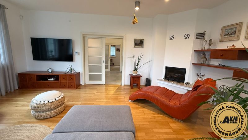 Living room of a family house with a fireplace, a comfortable chaise lounge, and a wooden decor floor.