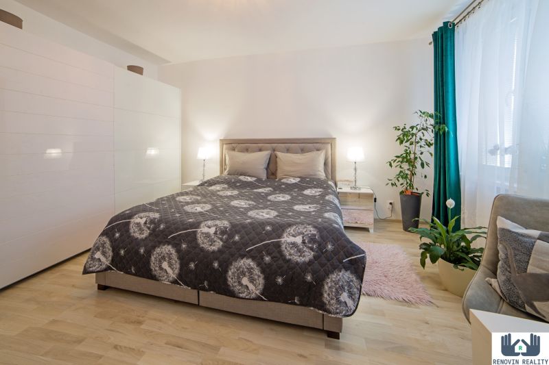 A bright bedroom with a large bed, wardrobes, and plants in a studio apartment, with a wooden decor floor.