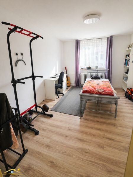 A bedroom with wood-patterned flooring, exercise equipment, and a work desk in a family house.