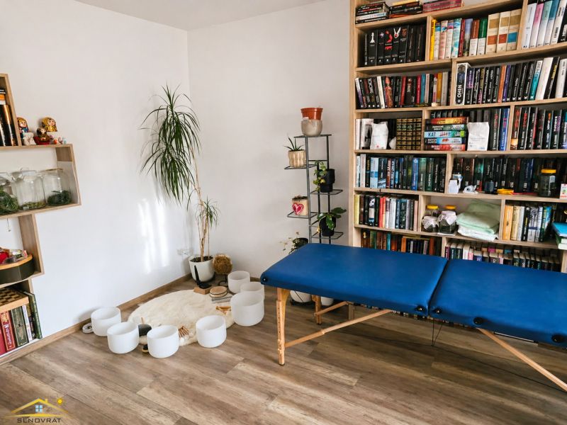 A room in a family house with a wooden decor floor, a bookshelf, and a massage table.