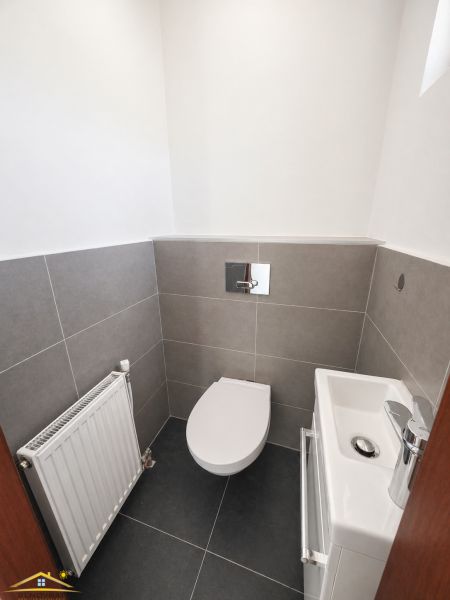 A toilet with a sink in a family house, with gray tiles on the walls and floor.