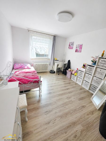 A room with a bed, a floor with a wooden decor, and decorations in a family house.