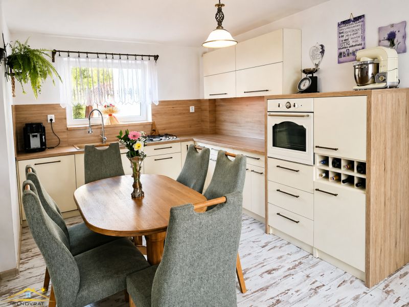 A kitchen in a family house with wooden decor, green chairs, a dining table, appliances.