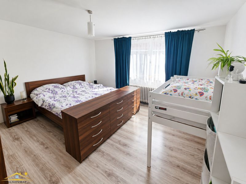 A bedroom in a family house with a bed, a bunk bed, and a wooden decor floor.