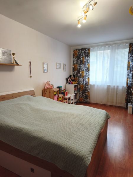 A bedroom in a 2-room apartment with a bed, decorative curtain, and floor with a wooden decor.