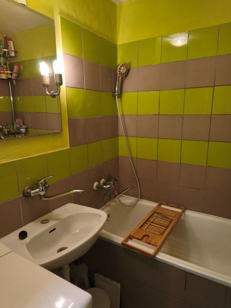 A bathroom with green-brown tiles and a bathtub in a 2-room apartment.
