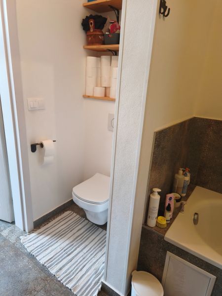 A bathroom in a 4-room apartment with a toilet, shelf, and bathtub, floor with wood decor.
