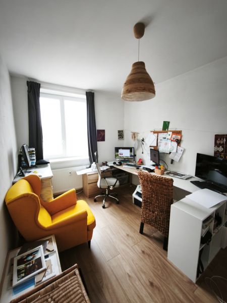 A home office with a yellow chair, wood-patterned flooring, and a large window in a 4-room apartment.