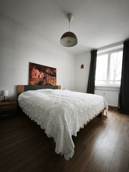 A bedroom with a bed, painting, wood-patterned floor, and curtains in a 4-room apartment.