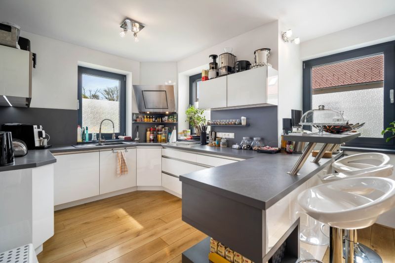 A kitchen in a family house with white furniture and a wooden decor floor.