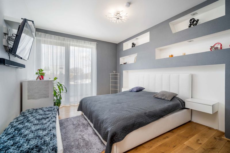 A bedroom in a family house with a wood-patterned floor, a gray wall, and a television.