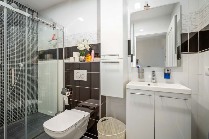 A bathroom in a family house with black and white tiles, a shower corner, and a cabinet under the sink.