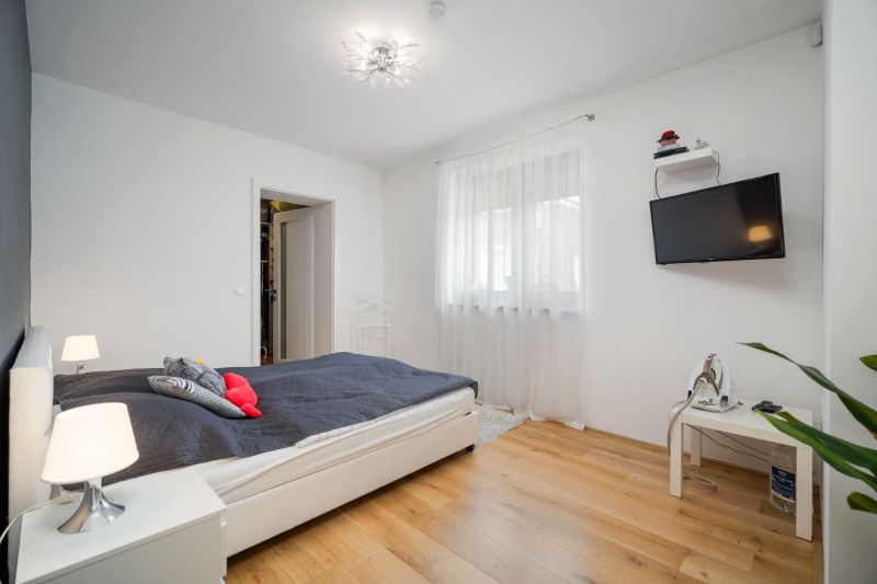 A bright bedroom with wood-decor flooring, a bed, and a TV on the wall in a family house.