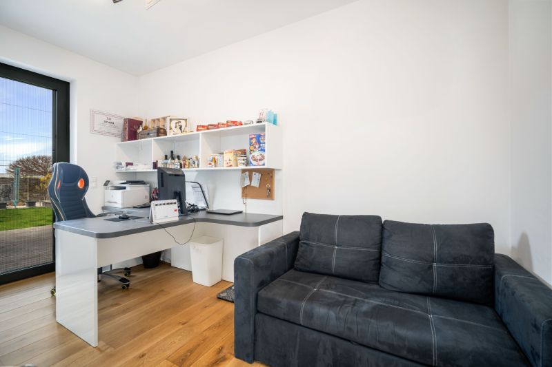 An office in a family house with a black sofa, a desk, and a wooden decor floor.