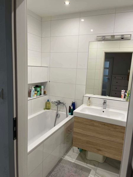 A bathroom in a 3-room apartment with a bathtub, a sink, and a floor with a wooden decor.
