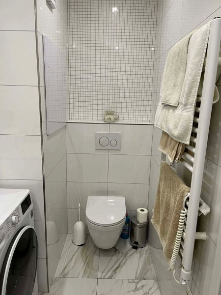 A bathroom in a 3-room apartment with a washing machine, tiles, and a wall-mounted toilet.