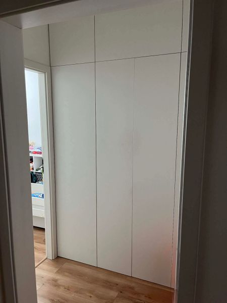 White built-in wardrobe in a 3-room apartment with a wooden decor floor.