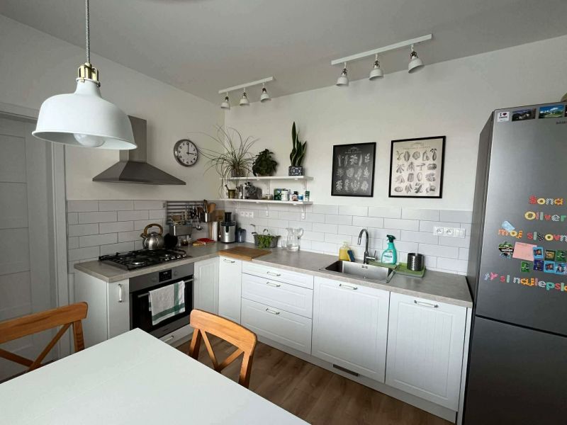 A kitchen in a 3-room apartment with white cabinets, a wooden decor floor, and decorations.